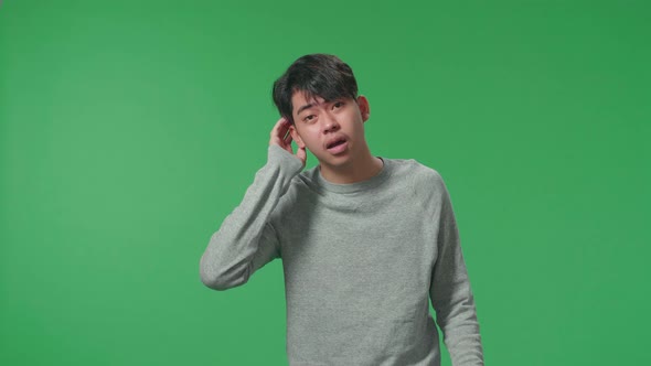 A Puzzled Asian Man Is Standing In Front Of Green Screen Background alt