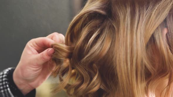 A Curl on the Head of a Girl with Brown Hair is Corrected By a Hairdresser Sprays with Varnish and