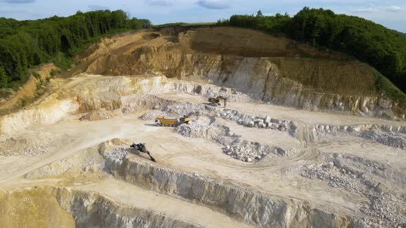 Open pit mining of construction sand stone materials with excavators and dump trucks.
