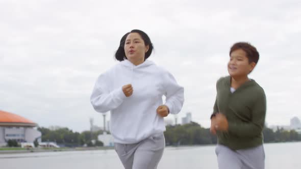 Athletic Asian Mother and Son Jogging Outdoors along Urban Riverside alt