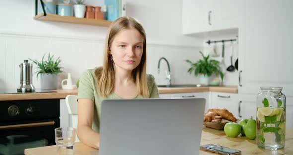 Young Business Woman Talks on Phone and Works on Laptop in White Kitchen
