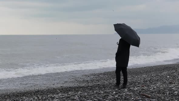 Man with umbrella standing on the beach by the sea