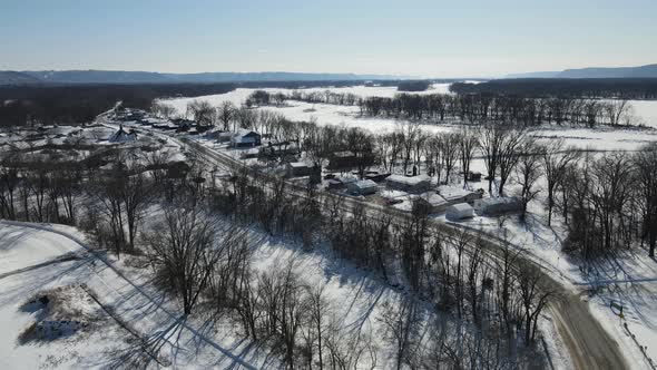 Aerial view of frozen river in snow covered valley with island with trees. Bright blue sky.