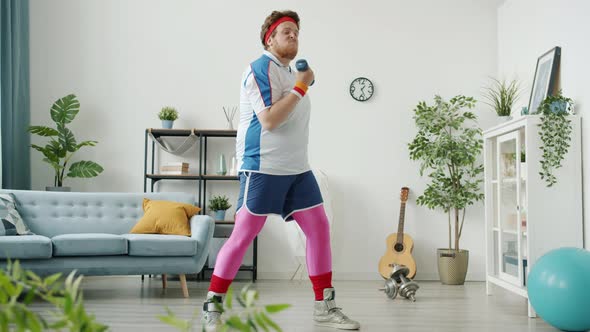 Slow Motion of Funny Fat Guy in Bright Clothing Exercising with Dumbbell and Eating Banana Looking alt