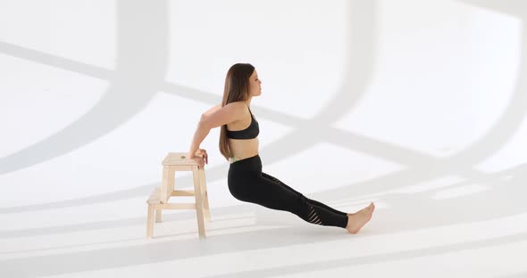 Side View of Young Caucasian Woman Working Out Doing Exercises in a White Studio