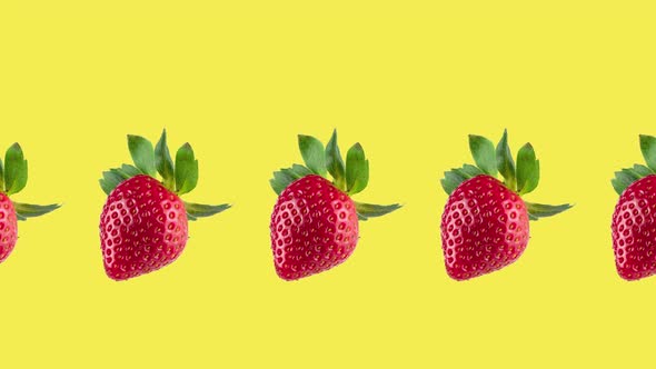 one line of fresh red strawberries rotating close-up on a yellow background