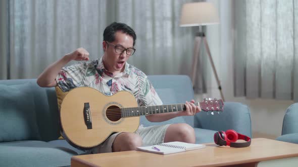 Asian Man Composer With A Guitar Celebrating For Finishing Composing Music On Paper At Home alt