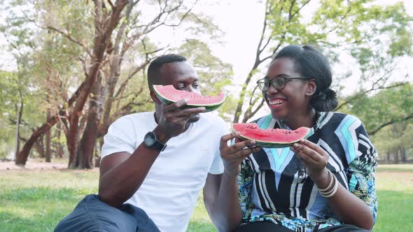 Happy African American Couple eating fresh watermelon during outside date in park