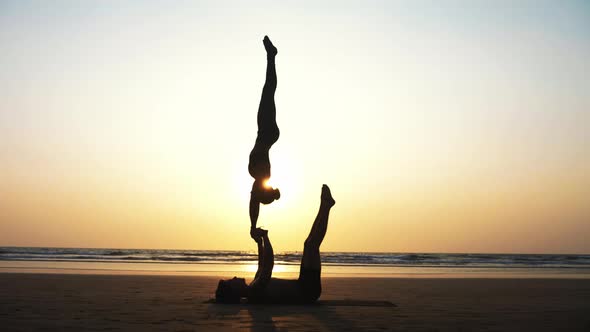Fit Sporty Couple Practicing Acro Yoga with Partner Together on the Sandy Beach alt