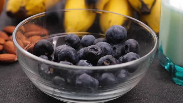Drops Fresh Blue Berry in Bowl with Banana Milk and Almond on Table alt