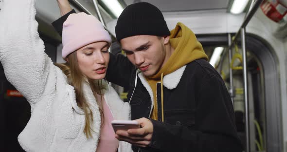 Millennial Couple Talking and Looking at Mobilephone Screen. Pretty Girl and Her Boyfriend Sharing alt