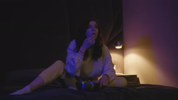 Young Beautiful Woman Sitting On A Cozy Sofa At Home At Night Eating Popcorn Watching TV alt