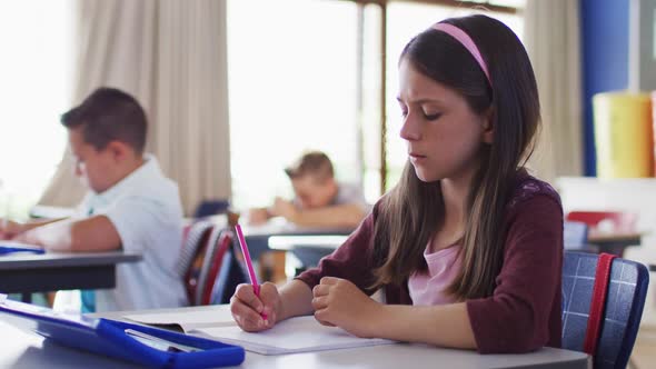 Portrait of caucasian schoolgirl sitting in classroom, making notes alt