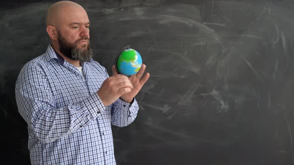 an Adult Bearded Caucasian Man in a Shirt Stands and Rotates the Globe alt