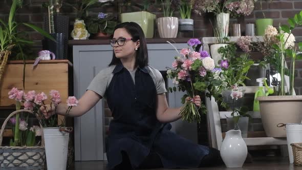 florist sits on floor of flower workshop and makes bouquet of roses  carnations alt