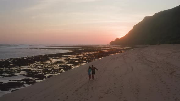 A Couple Walking Along Sandy Beach at Sunset