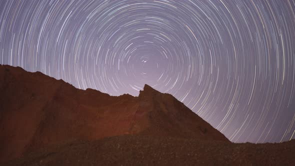 Video motion of night sky with circular star trails over the rock formations mountains foreground.