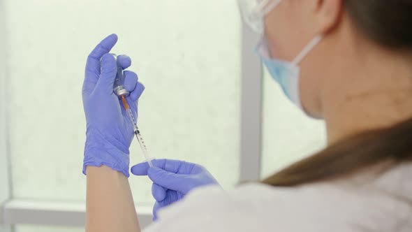 A Doctor in a Medical Mask and Blue Gloves Holds a Syringe and a Vaccine alt