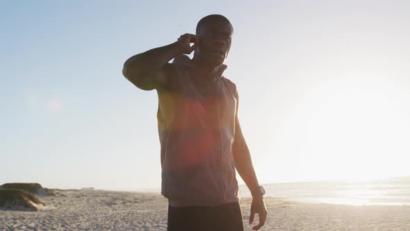 African american man checking smartwatch, exercising outdoors by seaside alt