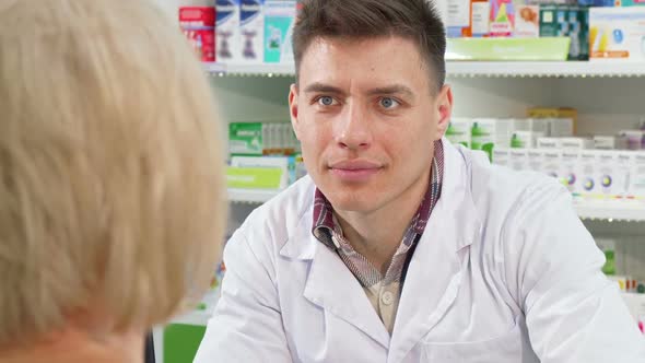 Male Chemist Listening To His Senior Female Customer Request on Medicine alt