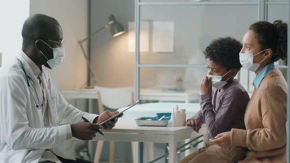 African American Boy and Mother in Masks Having Consultation with Pediatrician alt