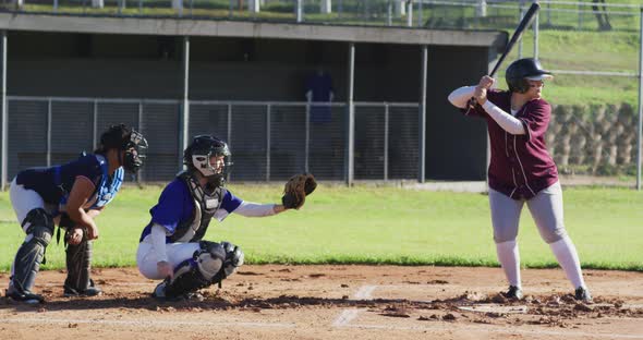 Diverse group of female baseball players playing on the field, hitter hitting pitched ball alt