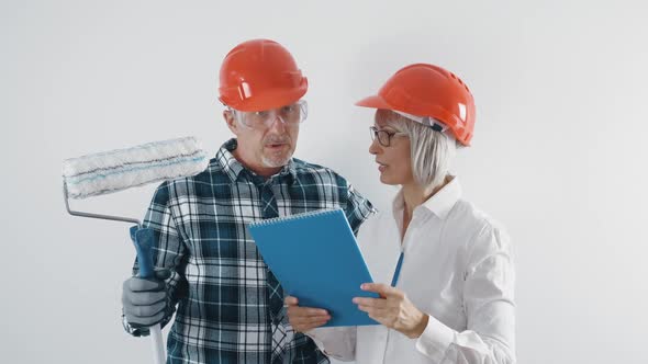 A Working Man and a Woman Engineer in Helmets with a Tablet Discuss Plans for the Reconstruction of