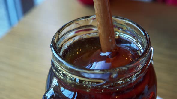 A Woman Stirs Honey in a Glass Jar with a Honey Dipper - Closeup alt
