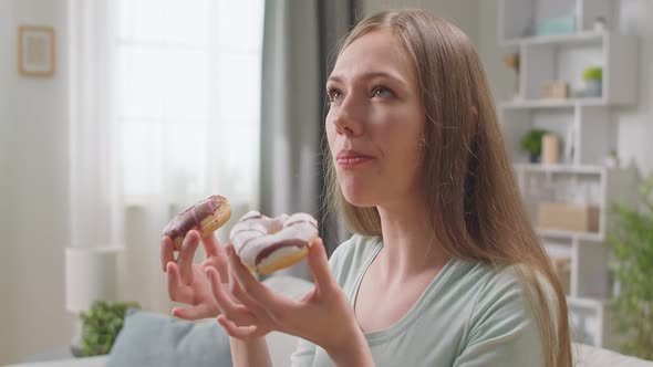 Cheerful Girl Appetizingly Eats a Two Donut at Home on the Sofa alt