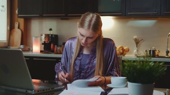 Blonde Business Woman in Bathrobe Signing Documents in the Kitchen at Home alt