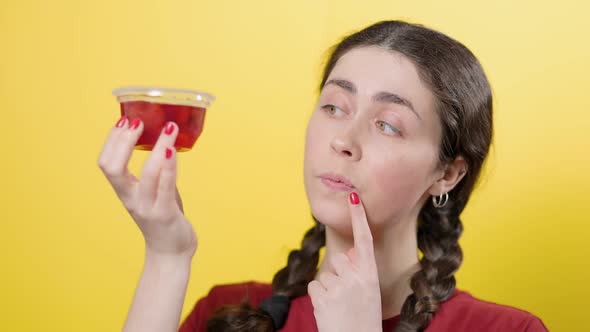 Portrait of a young smiling woman looking thoughtfully at a jar of jelly. alt
