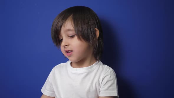 Boy Child in a White Tshirt is Sitting on a Bed Against a Blue Wall and Playing alt