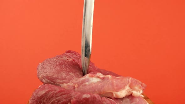 A large knife is stuck into a piece of red meat on a bright orange background. alt