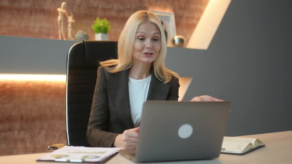 Friendly Caucasian Mature Elegant Woman Top Manager Ceo Sit in Office Using Laptop Talking By Video alt