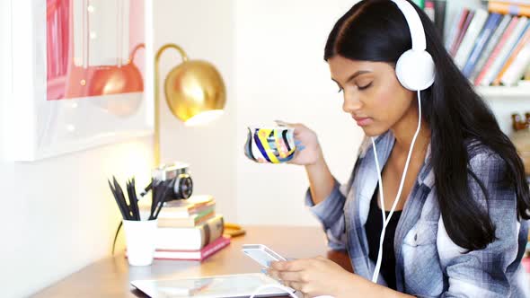Woman using mobile phone while having cup of coffee alt