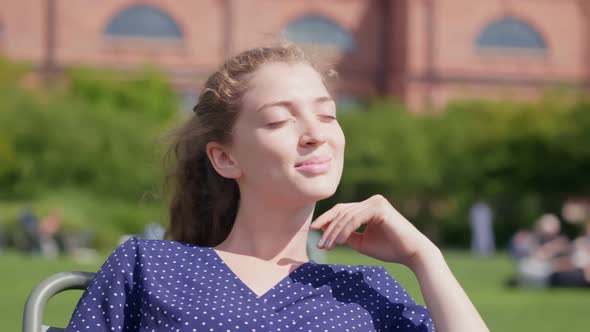Portrait of a Young Beautiful Woman Sitting on Chair in Park alt
