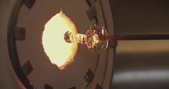 Professional glassblower working the oven with a piece of glass design alt