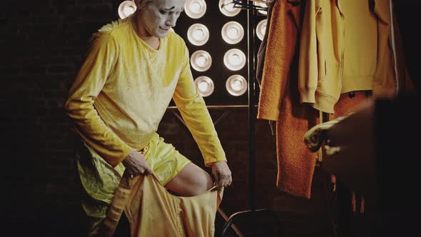 Mime Puts on Yellow Stage Costume for Performance in Circus alt