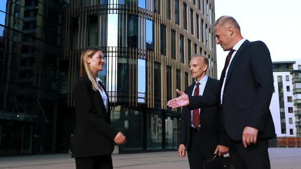 Two Businessmen Meet a Businesswoman and Shake Hands with Her Then Talk Together. Modern Office