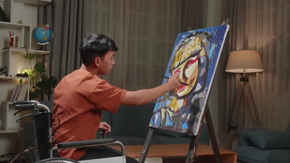 Asian Artist Boy In Wheelchair Holding Paintbrush Painting A Girl's Face On The Canvas alt