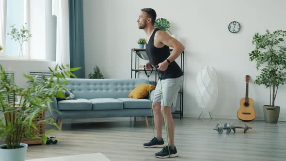 Slow Motion of Handsome Young Man in Sportswear Training with Stretch Band at Home alt