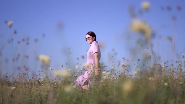 Girl in Purple Dress Walks Through the Field with Field Flowers. alt