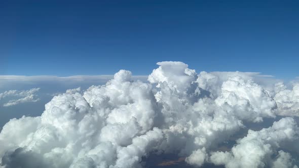 Stunning pilot view from a jet cockpit avoiding stormy cumulus clouds in a messy and deep blue sky alt