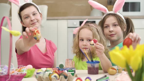 Three Beautiful Girls Show Drawings on Easter Eggs in Front of the Camera