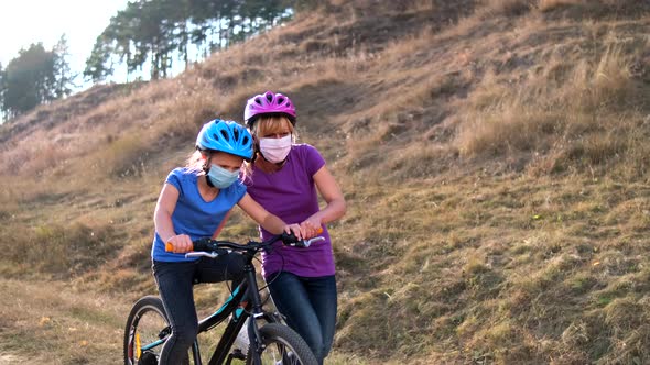 A young mother teaches his daughter to ride a Bicycle in medical masks and a Bicycle helmet