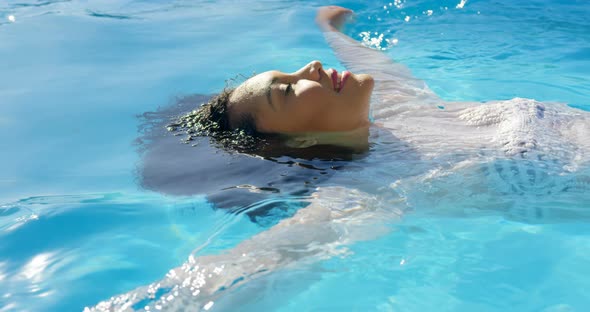 Side view of young mixed-race woman floating in swimming pool on a sunny day 4k alt