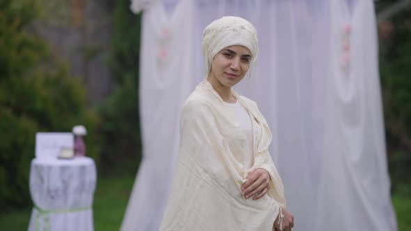Medium Shot Side View of Smiling Happy Middle Eastern Bride in Hijab and Wedding Dress Standing in alt