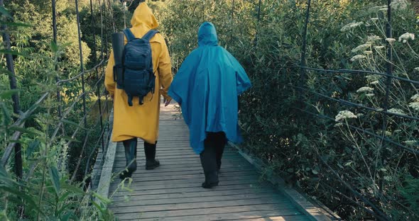 Man and Woman Hiker in Raincoats Walk on Suspension Bridge