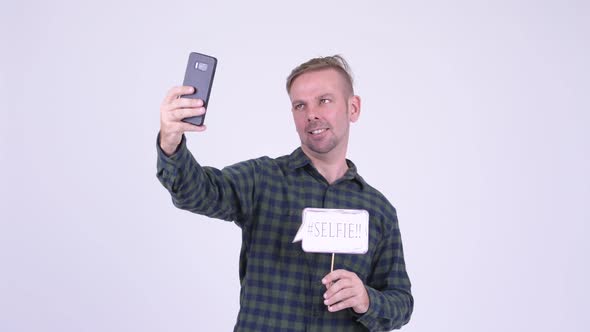 Portrait of Happy Blonde Hipster Man Taking Selfie with Paper Sign alt