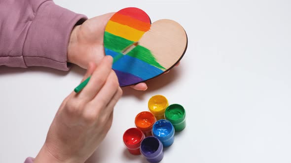 Hand Paints a Wooden Heart in Colors of Gay Pride Flag